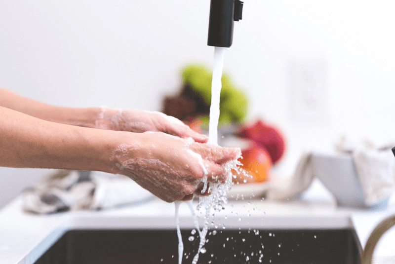Hands being washed under running water from a sink faucet, highlighting water quality and skin health.