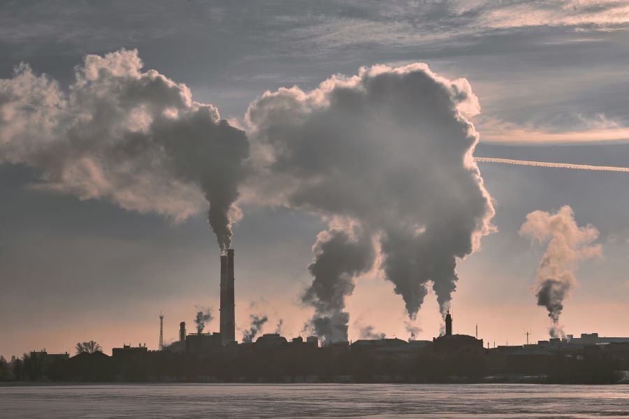 Silhouette of industrial buildings under white clouds of smoke during daytime, symbolizing air pollution and its effects on skin health.